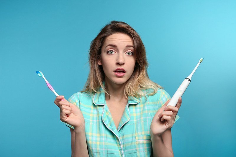 Young woman choosing between manual and electric toothbrushes.