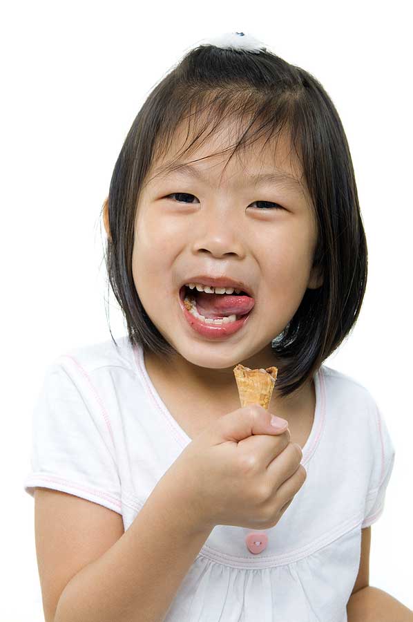 Young girl eating an ice cream cone, with her tongue sticking out to catch the crumbs.