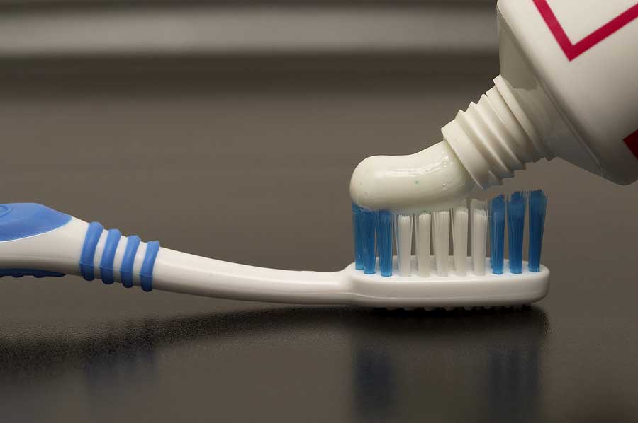 Toothpaste from tube is being dispensed onto the top of the toothbrush bristles