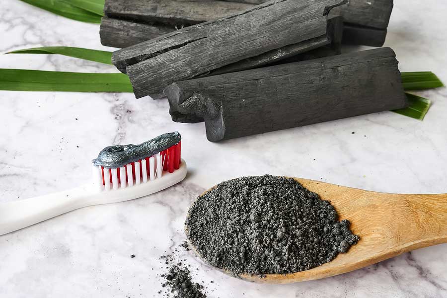 A toothbrush with charcoal toothpaste applied, laying next to a spoonful of activated charcoal.